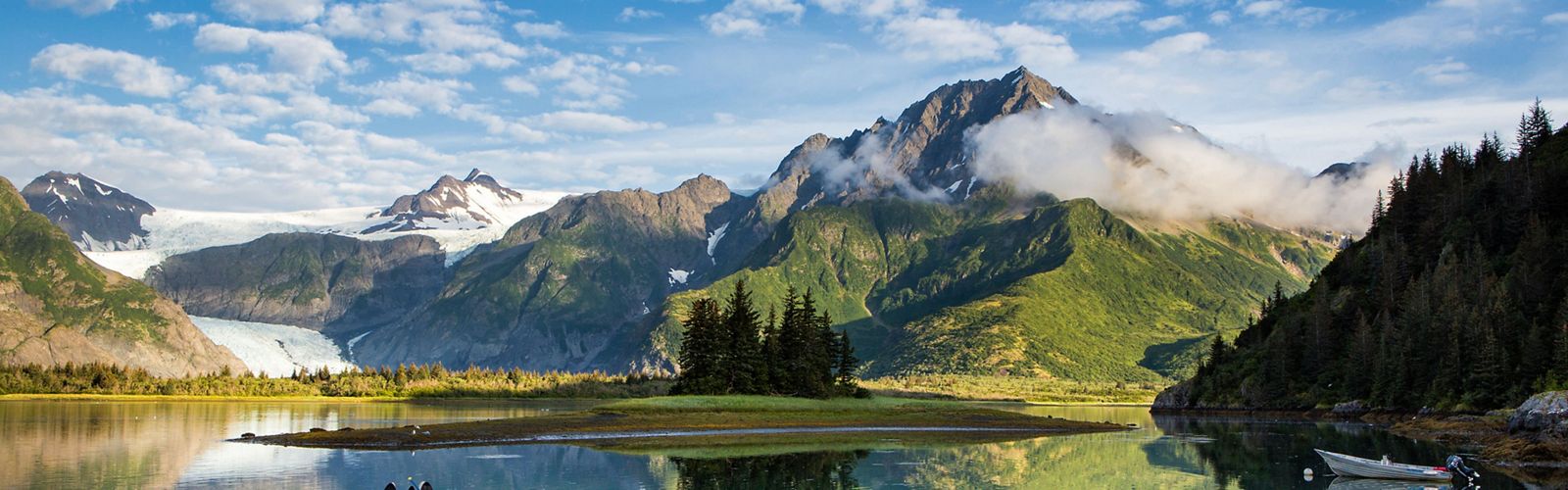 Fog-shrouded, snowy mountains in the background with a placid body of water in foreground.